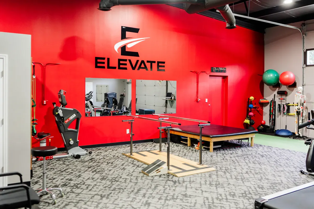 Inside the Elevate Physical Therapy clinic with the red Elevate wall and treatment equipment